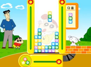 짱구 핵사 퍼즐 짱구교실 게임에서 공원 배경 퍼즐판 안에 색깔 블록이 바닥에 깔리고 일부가 기둥처럼 솟아 있으며 상단에는 떨어지는 블록과 다음 블록 창을 짱구와 강아지가 지켜본다.