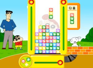 짱구 핵사 퍼즐 짱구교실 게임에서 공원 한가운데 세로 퍼즐판 안에 색깔 블록들이 층층이 쌓여 있고 상단에는 떨어지는 블록과 다음 블록 창이 보이며 짱구와 강아지가 양옆에서 지켜본다.